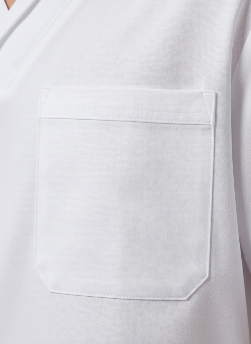 An elegant product detail shot of a white medical scrub top’s pocket and stitching, presented in photographic realism. The camera is positioned very close, focusing on the right chest pocket where a pen slot and reinforced edges are clearly visible. The fabric’s matte surface shows fine weave texture, and the double-stitched seams are straight and precise. Soft studio lighting from the top right creates subtle shadows along the pocket edges and emphasizes the slight lift of the fabric around the stitching. The background is a softly blurred continuation of the same garment, keeping attention on the craftsmanship. The composition is minimalist and carefully cropped, evoking professionalism and quality for a medical clothing brand emphasizing durability and thoughtful design elements.